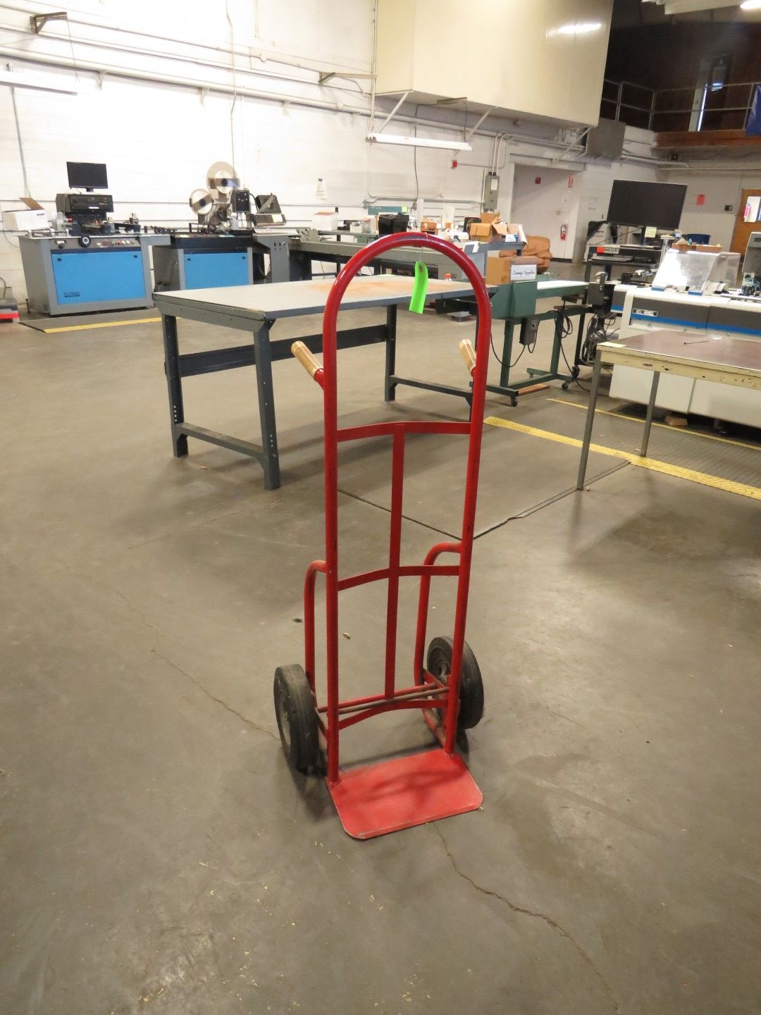 Red hand truck in a workshop setting with workbenches and equipment.