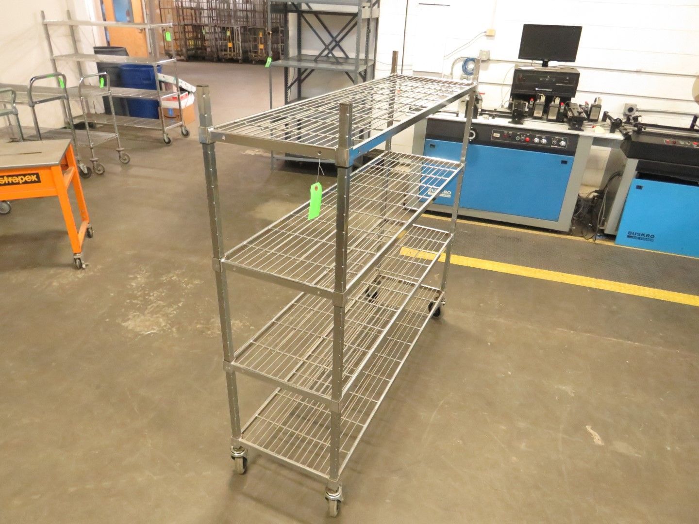 Stainless steel shelving unit on wheels, with four wire shelves, in a warehouse setting.