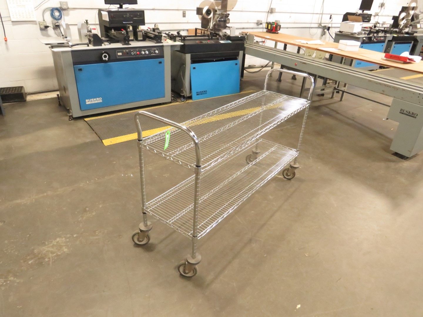 Wire shelving cart in a workshop setting with machinery in the background.