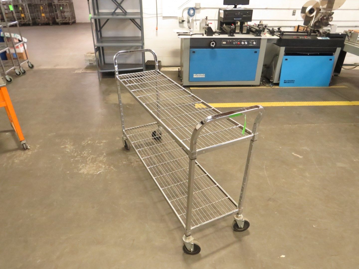 Two-tiered metal cart with wire shelves, on wheels, in a warehouse setting.