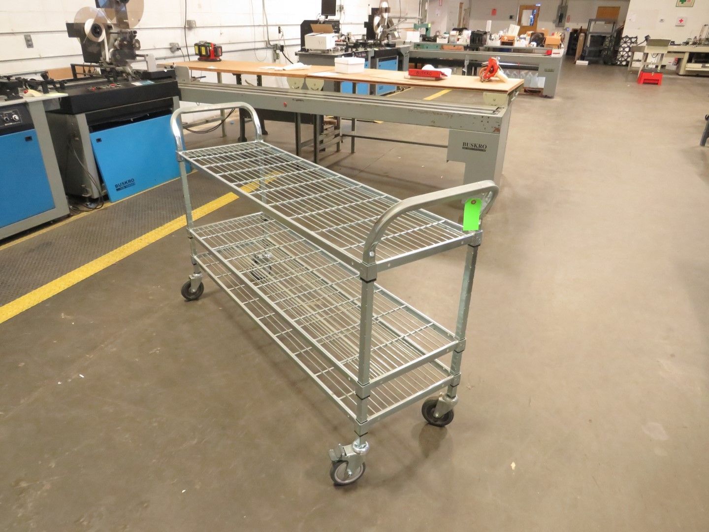 Metal wire shelving cart on wheels in a workshop, two shelves visible.