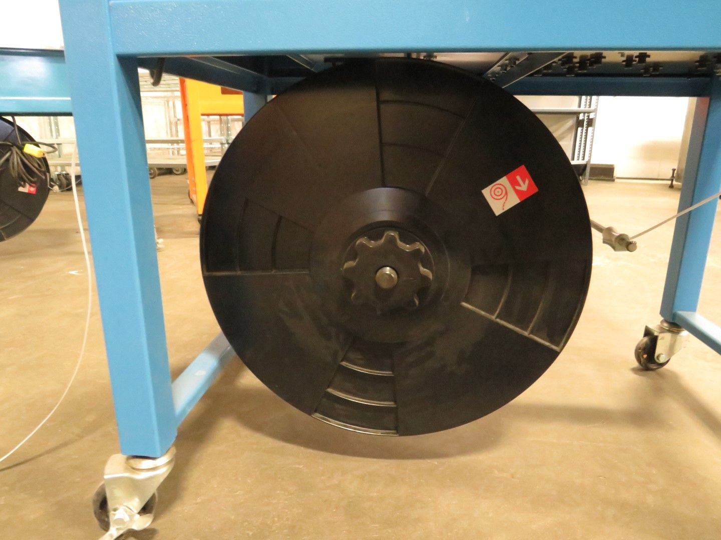 Black, circular industrial part attached to a blue metal frame with a sprocket in its center.