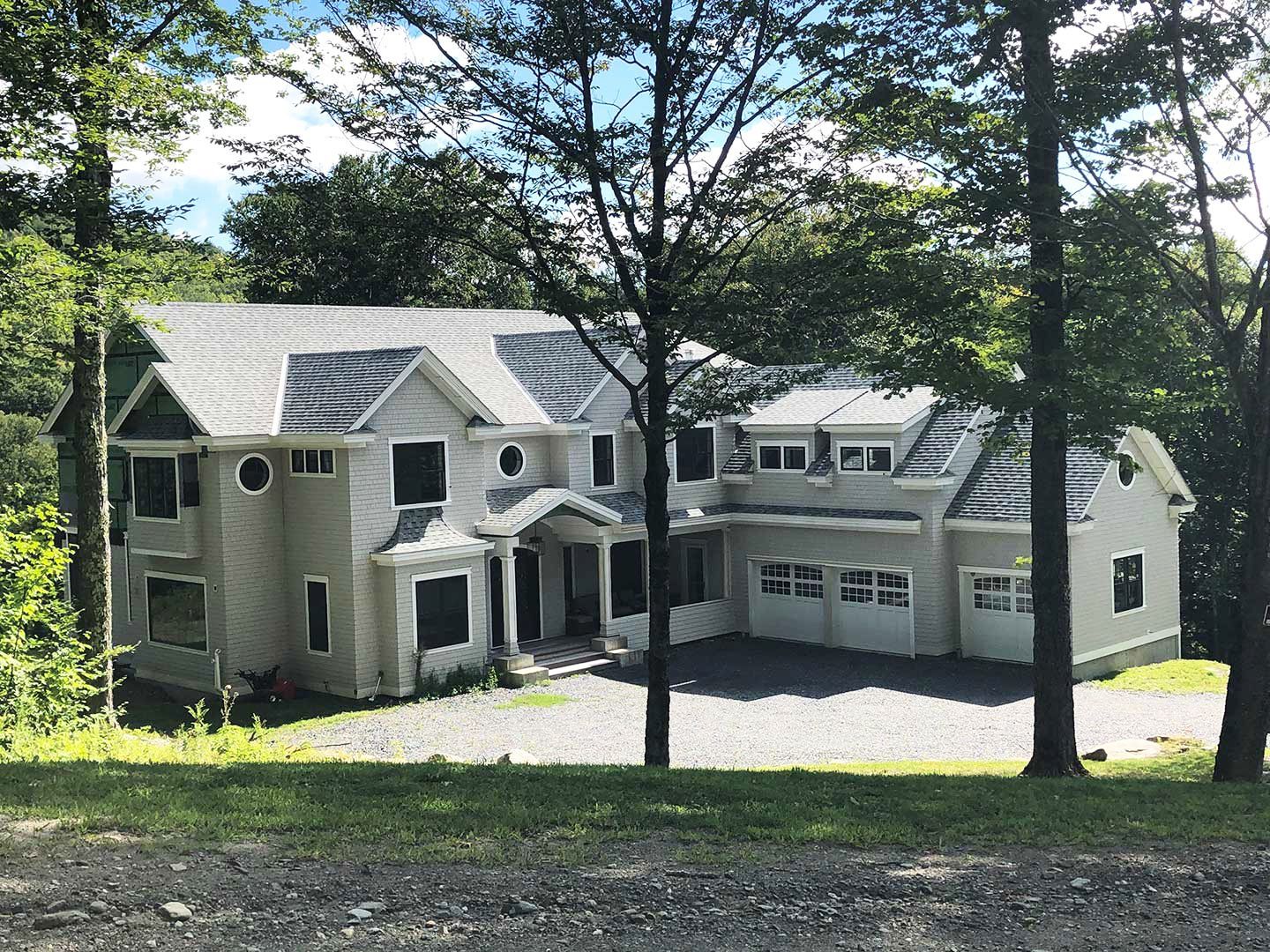 Two-story light-colored house with attached garage, nestled among trees on a hillside.
