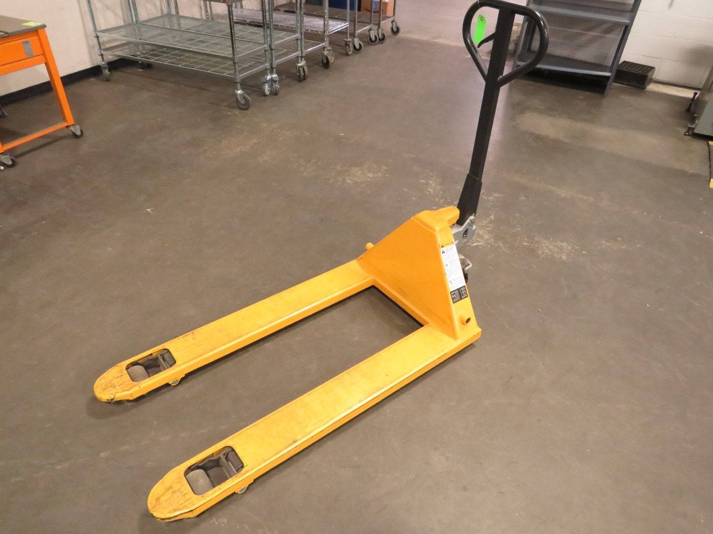 Yellow pallet jack on a gray concrete floor, handle upright.