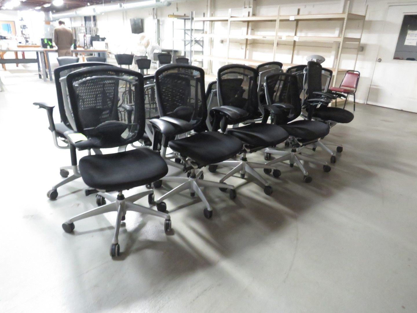 A cluster of black mesh office chairs with silver bases in a warehouse setting.