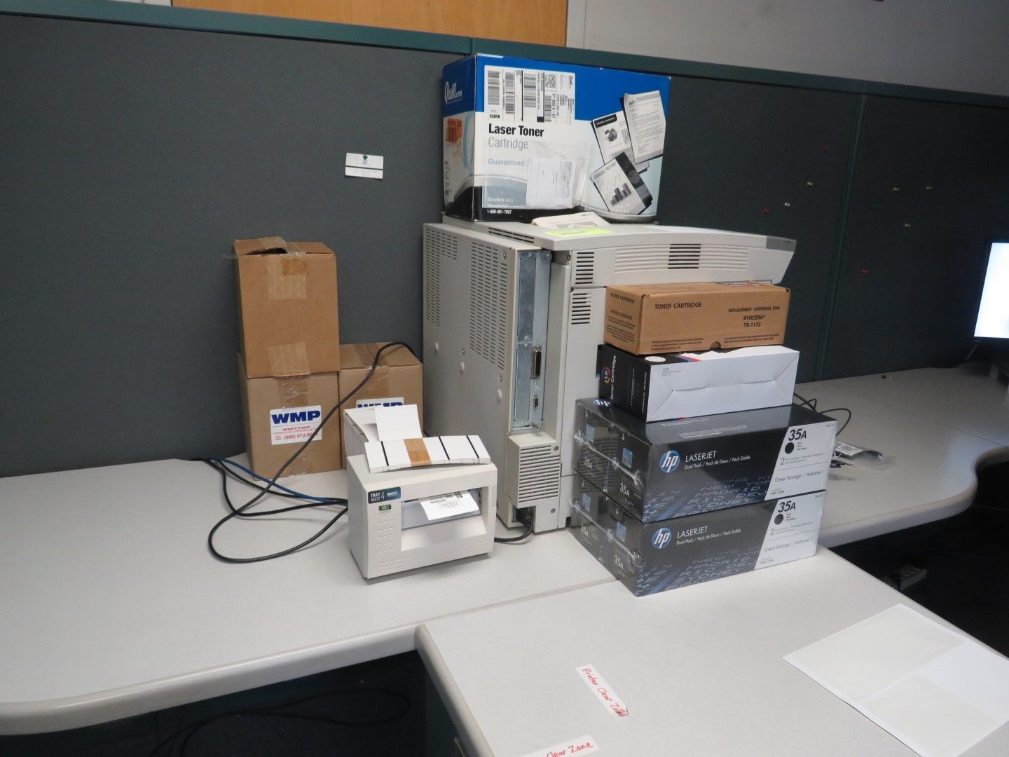 Boxes, computer tower, and small printer on a white desk in a workspace.