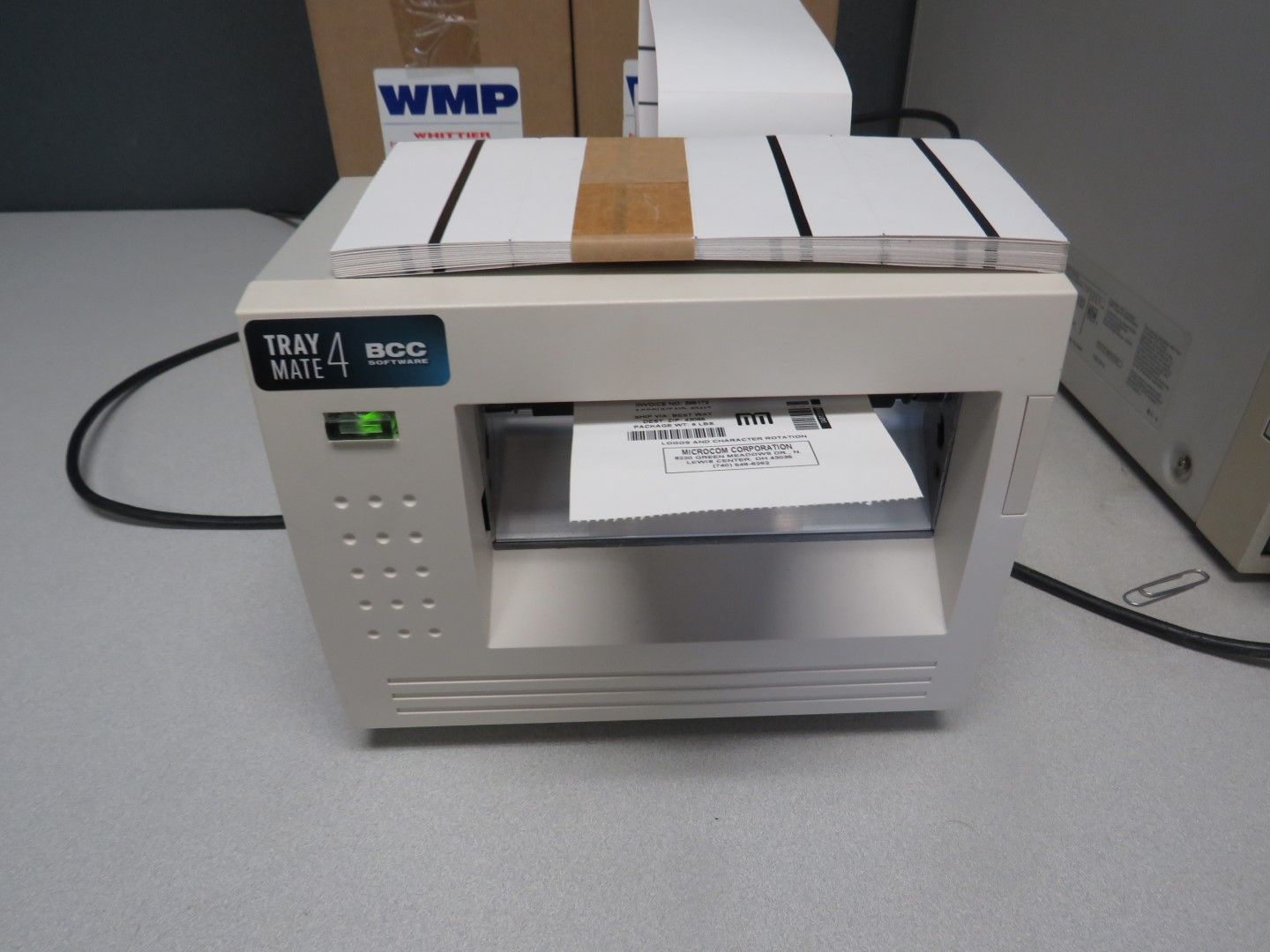 A label printer with a printed label emerging. White machine, white labels on top, on a white desk.