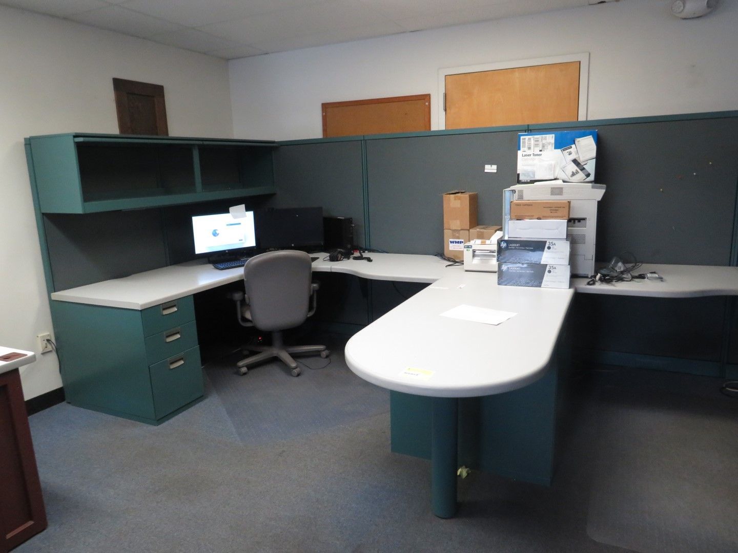 An office cubicle with a teal desk, computer, and chair.