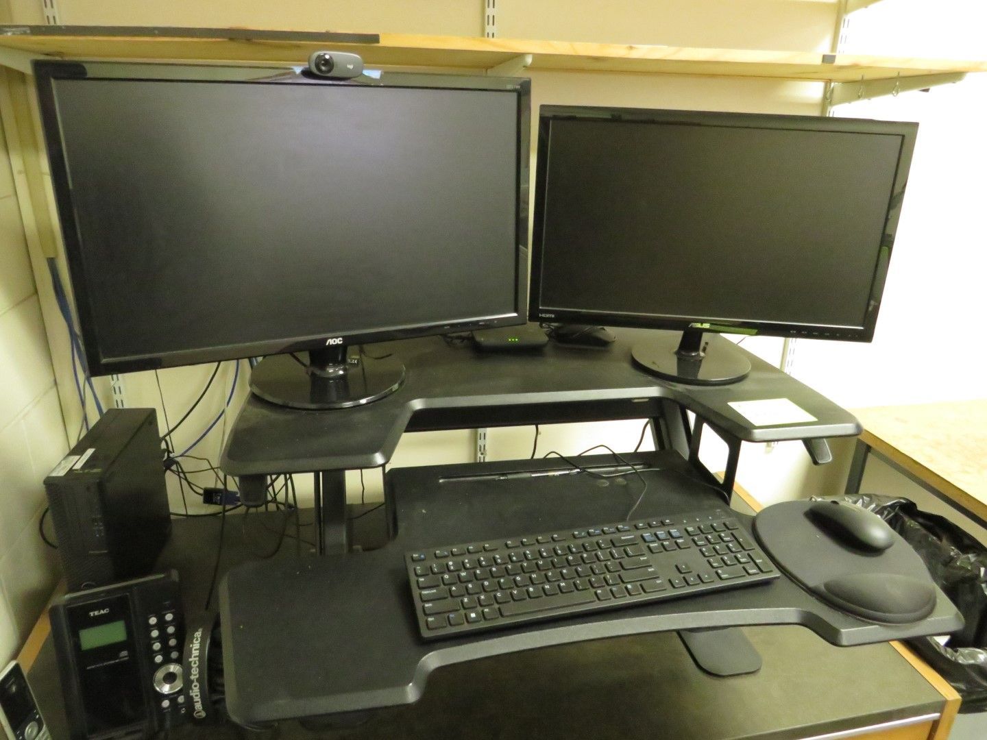 Dual-monitor desk setup with keyboard, mouse, and webcam. Includes a telephone and a computer tower.