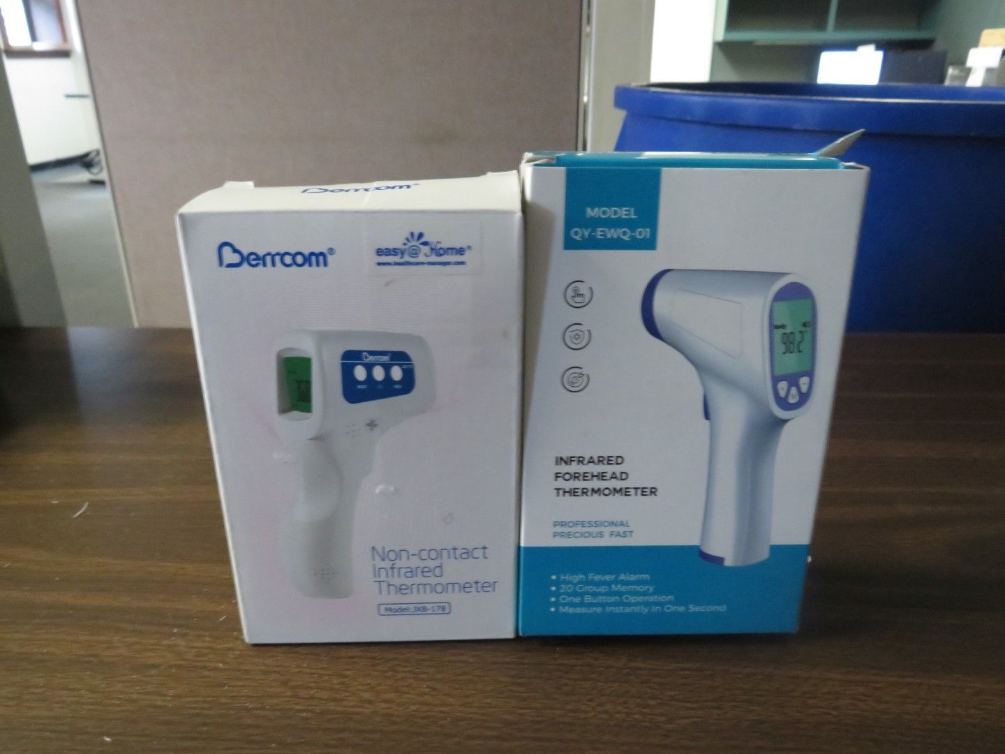 Two boxes of infrared thermometers on a table. One is white with a blue thermometer picture, the other is teal.