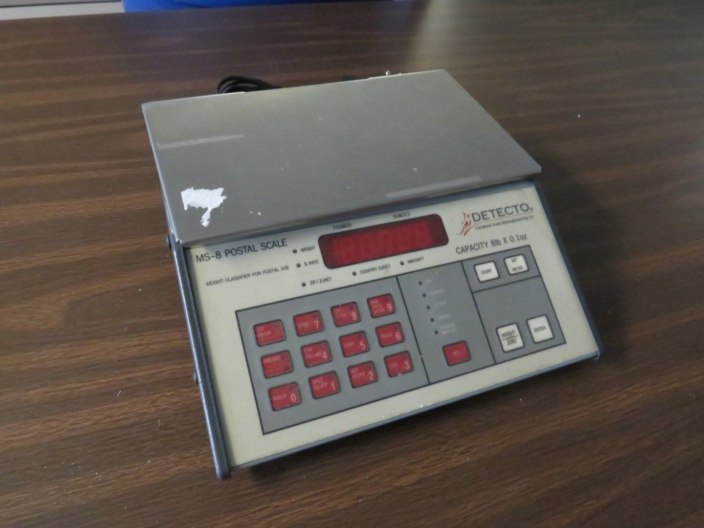 Gray and beige Detecto scale on a wooden table, with red display and keypad.