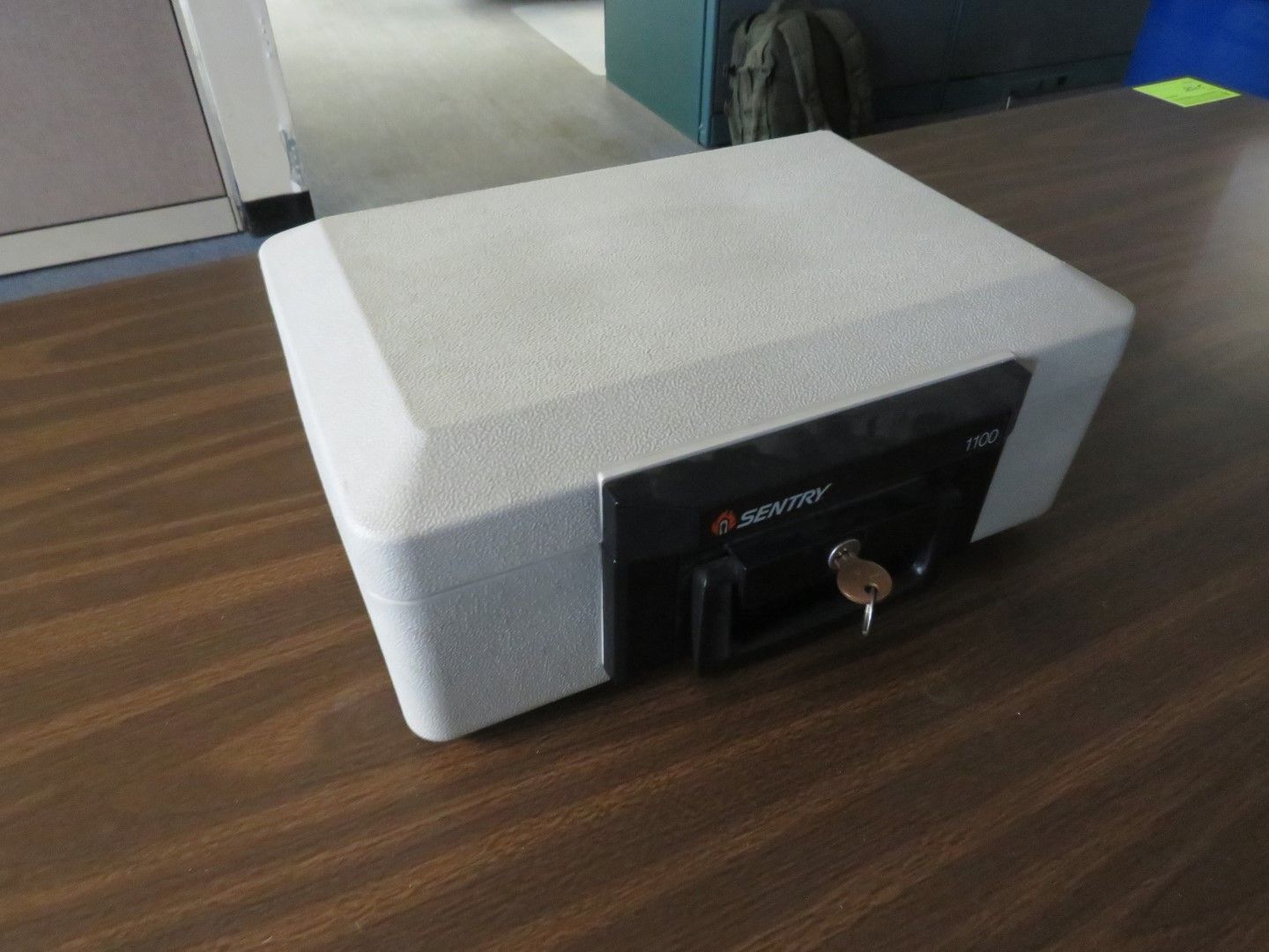 White and black safe box with a key, sitting on a brown table.