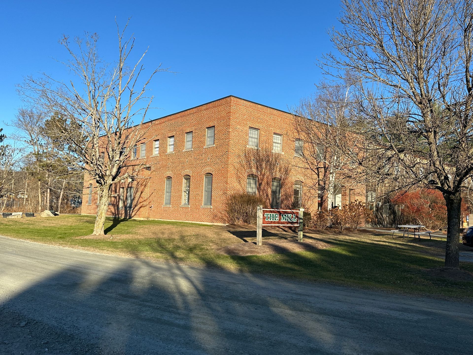 Brick building under a clear blue sky, flanked by trees with bare branches, on a grassy plot.