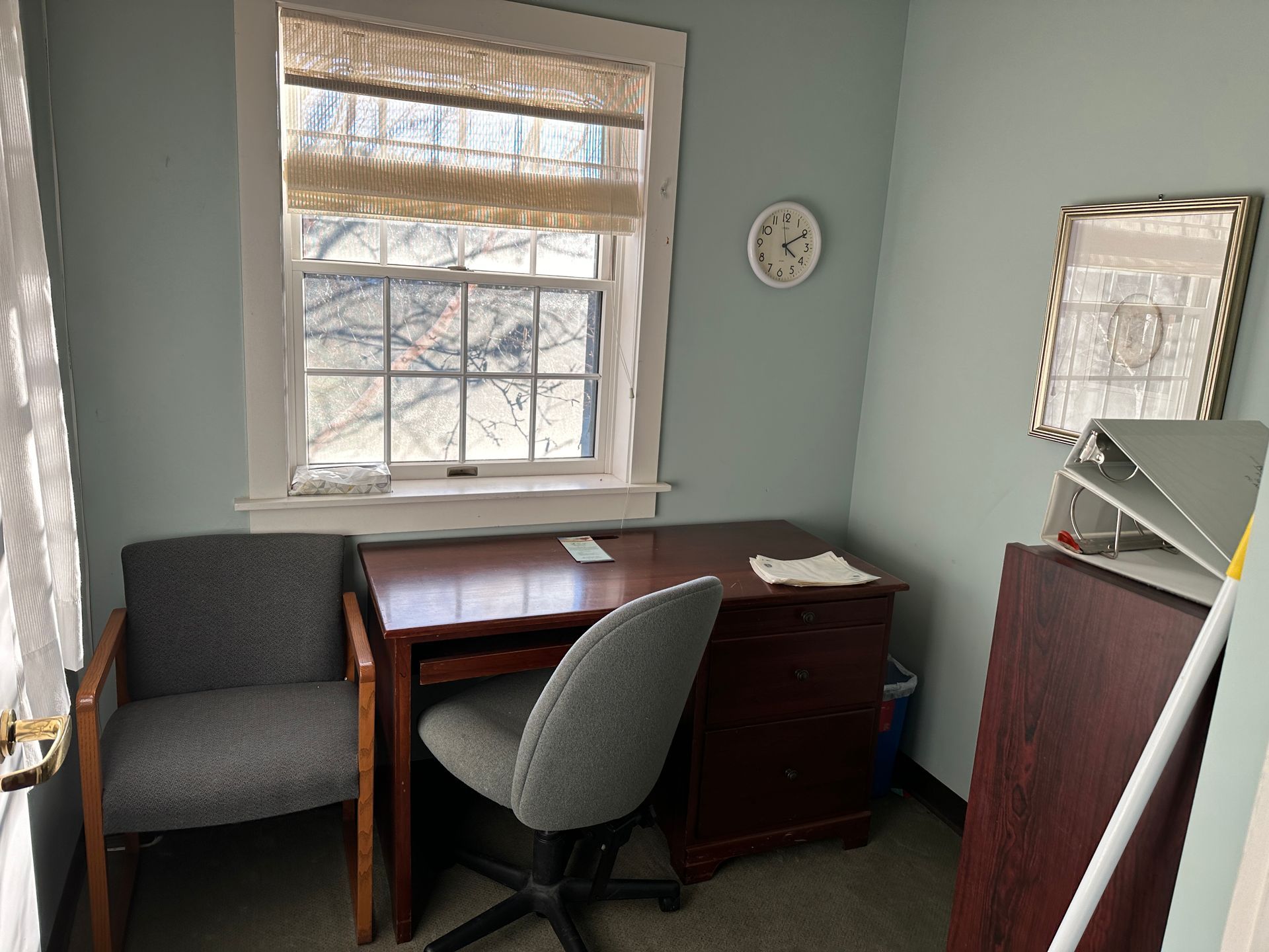 Small office with desk, chair, window, clock, and filing cabinet; walls are blue.