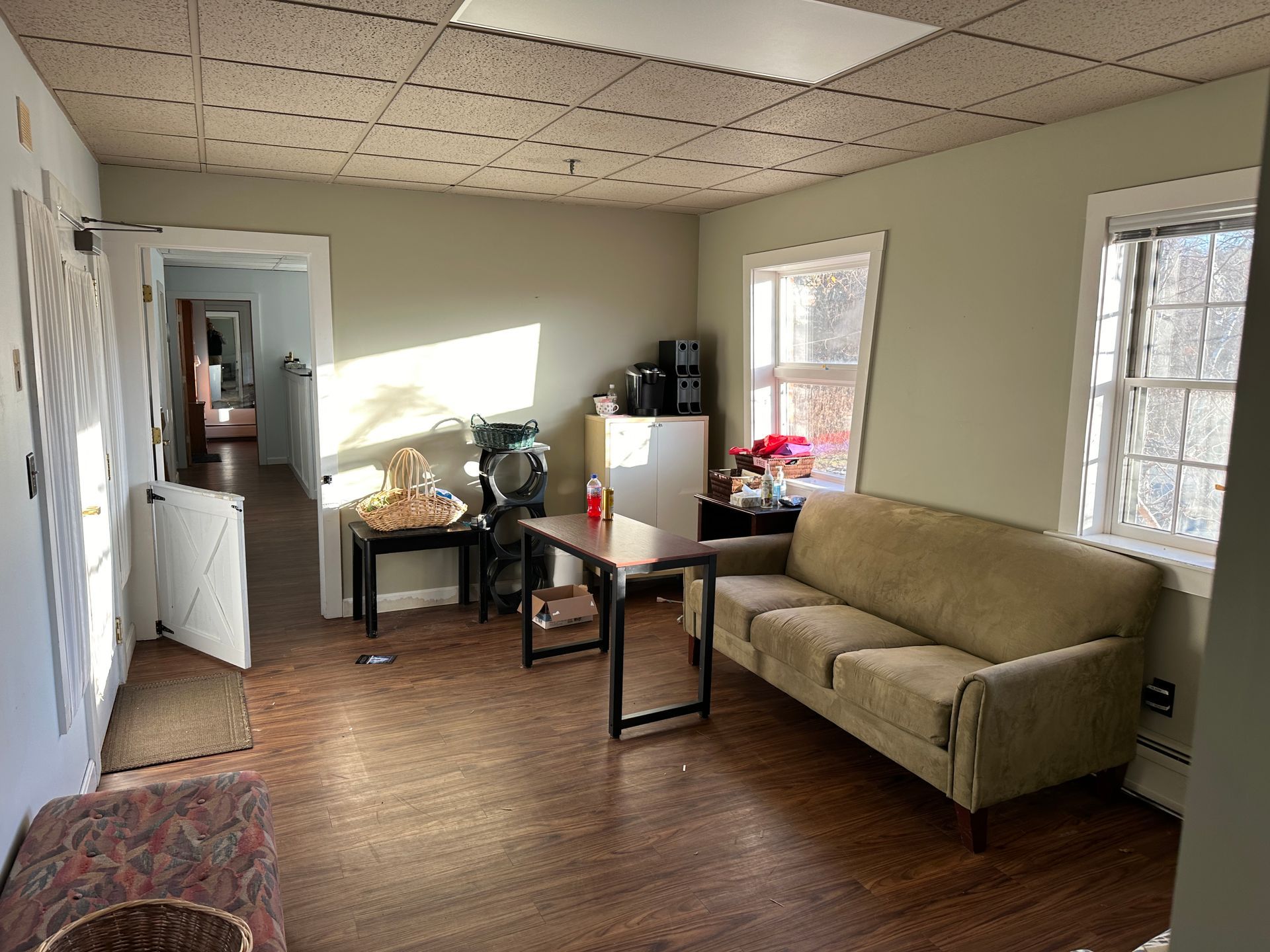 A furnished room with a couch, table, and windows; a doorway leads to a hallway.
