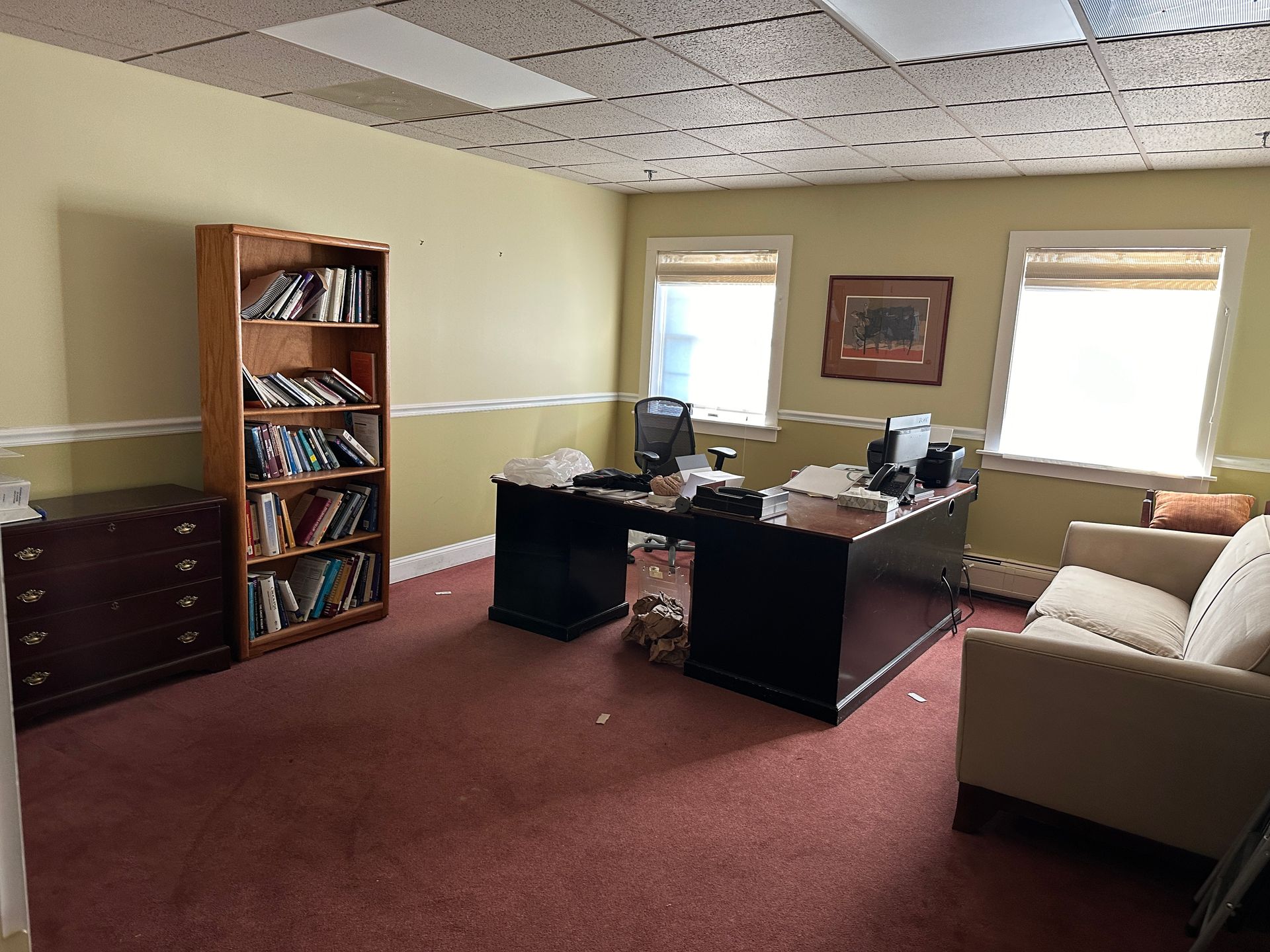 Office with desk, bookshelves, two windows, two chairs, and red carpet.