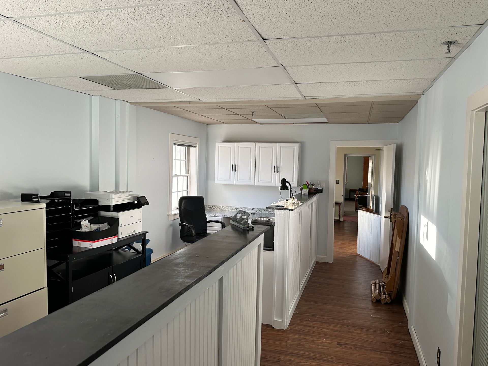 Office interior with light blue walls, a dark counter, and a hallway leading to another room.