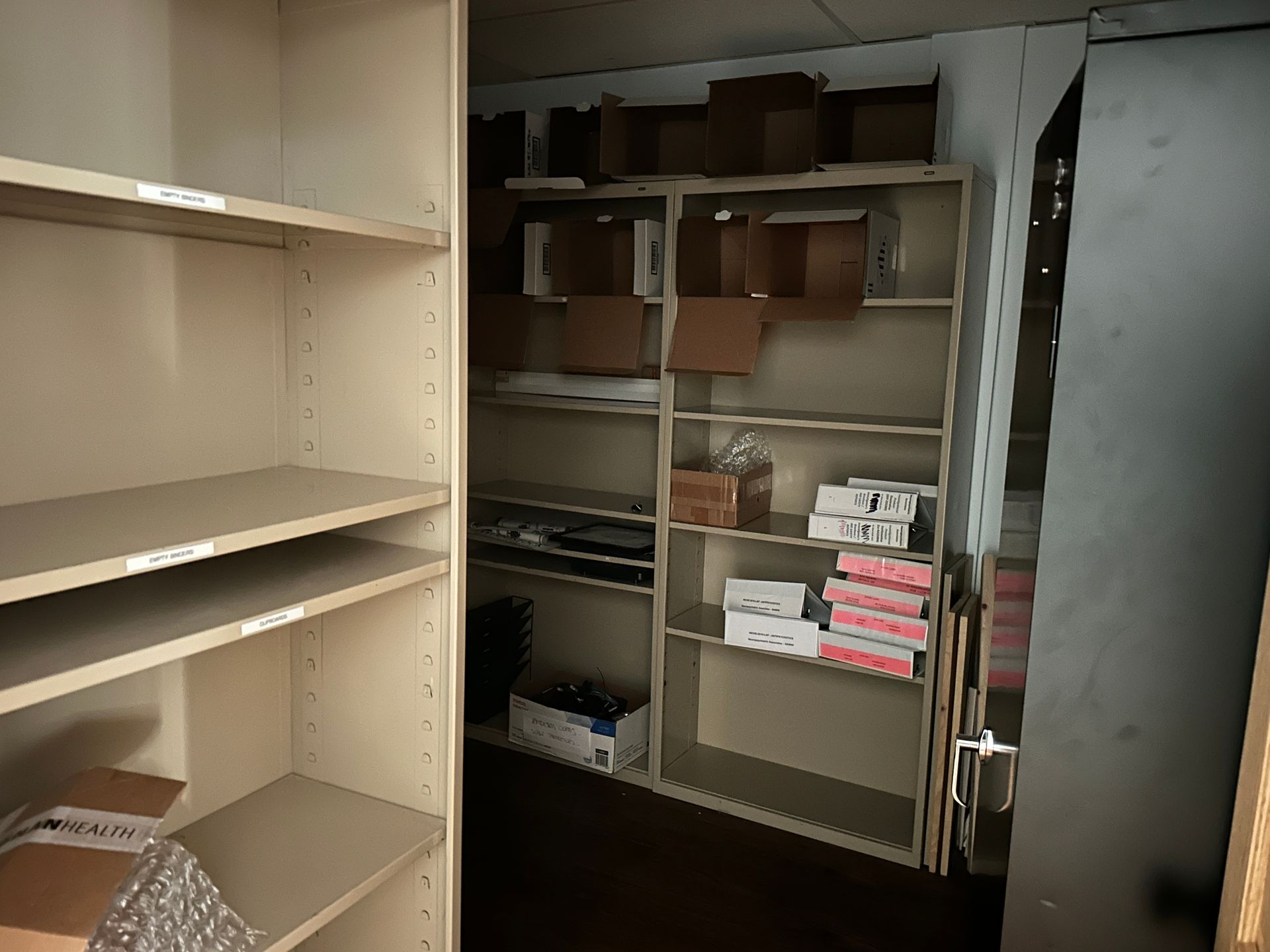Shelving unit storage room with empty and filled shelves; boxes, supplies.