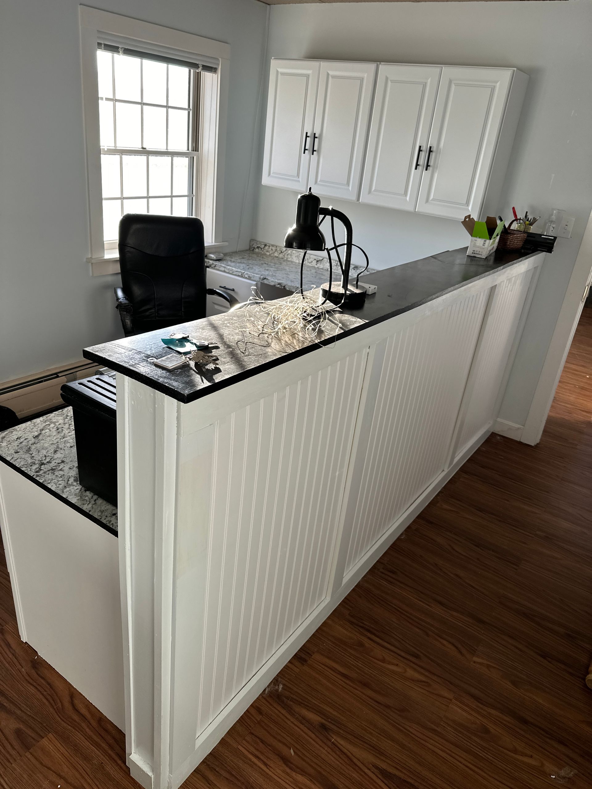 White and black office desk with cabinets, a black chair, and a window.