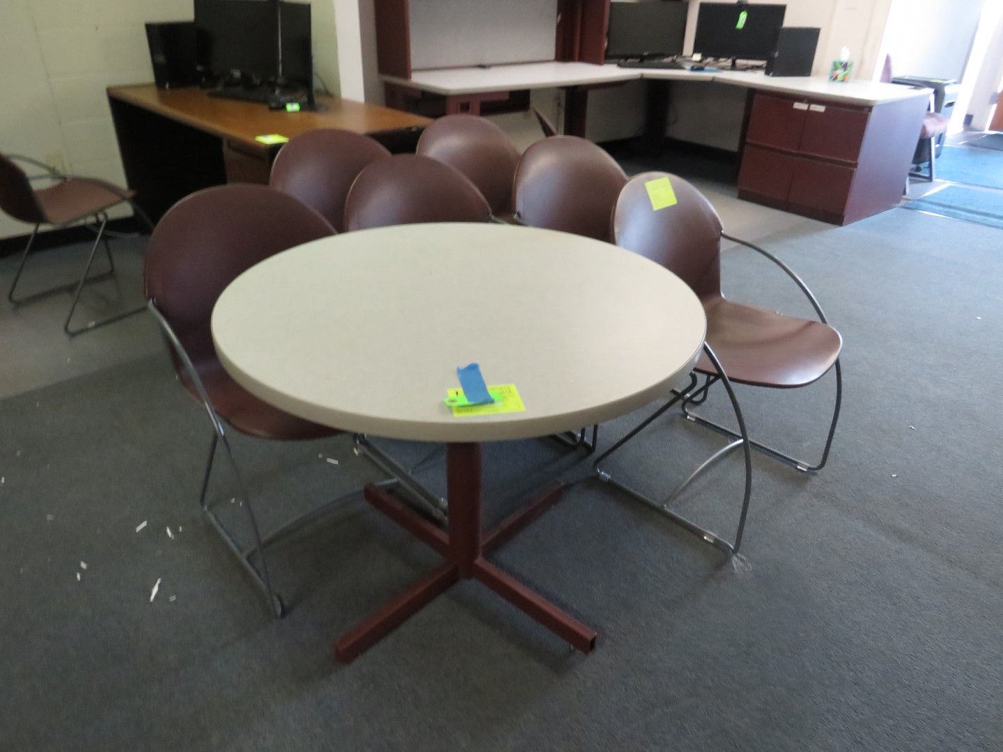 Round table surrounded by brown chairs in an office setting, with desks in the background.