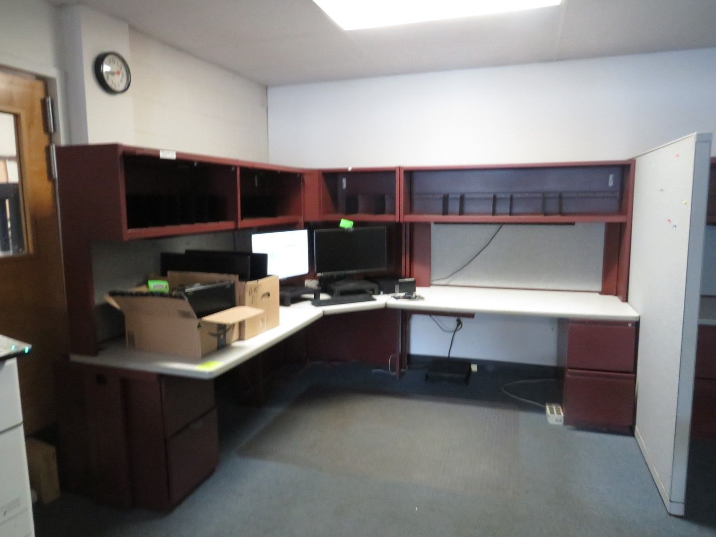L-shaped office desk with dark red cabinets, white desk surface, computer, and cubicle walls in a room.