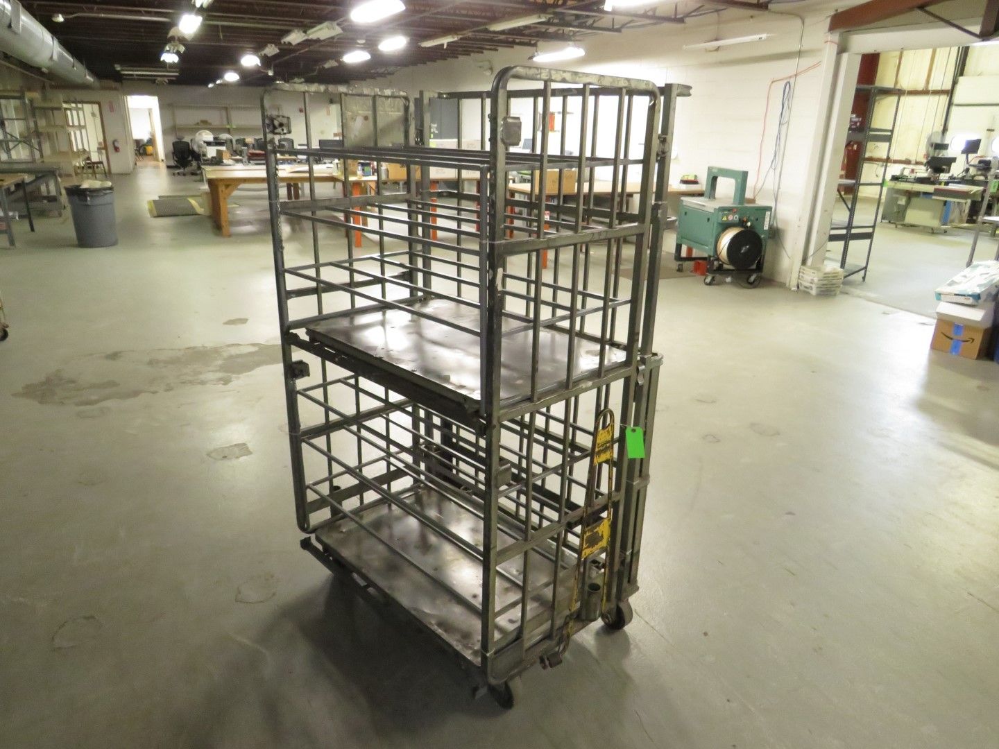 Metal cage cart with three shelves, sitting on wheels, in a warehouse.