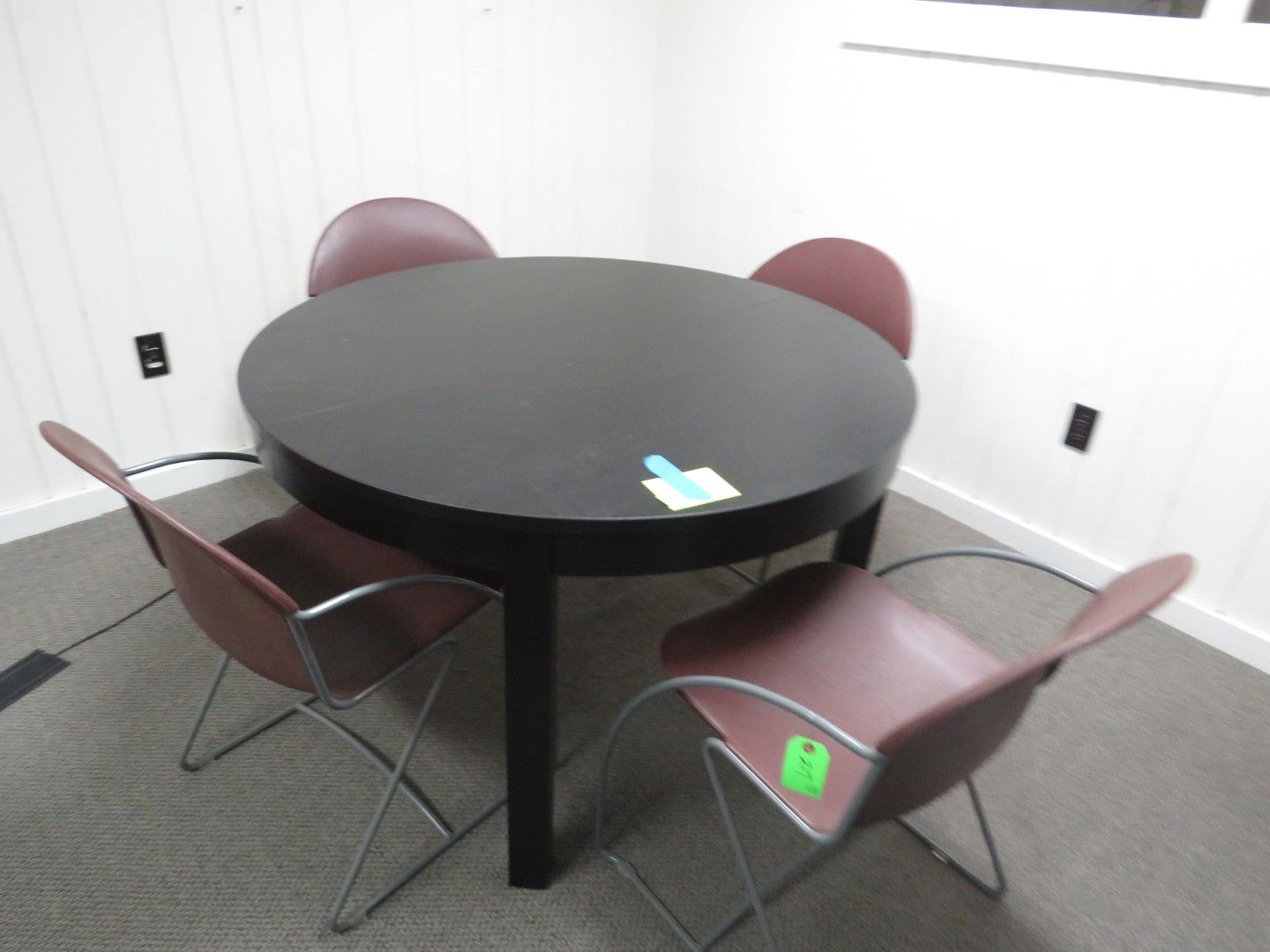 Round black table with four maroon chairs in a room with white walls and carpet.