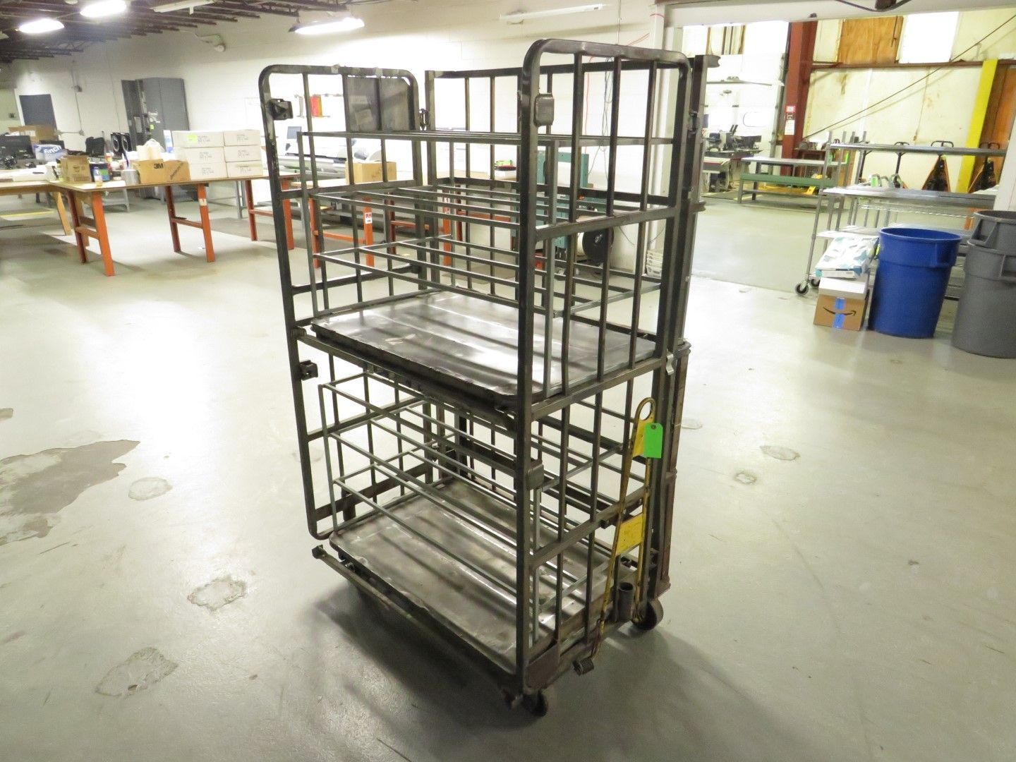 Metal storage cart with three shelves on wheels inside a warehouse.