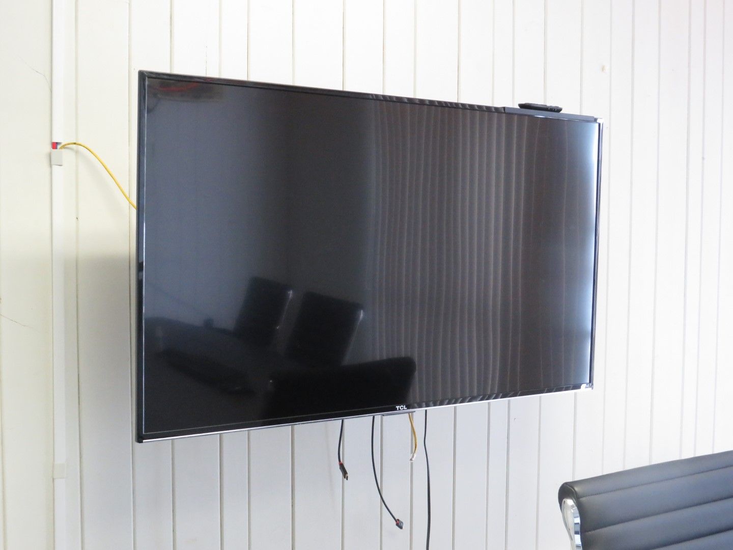 Large black TV mounted on white paneled wall with wires visible.