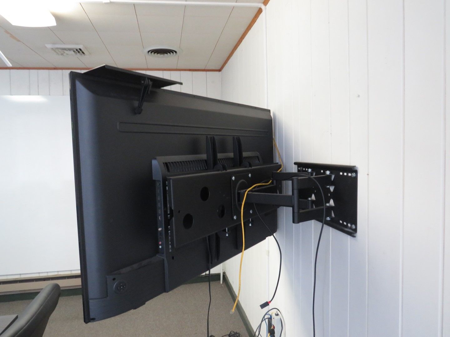 Black flat-screen TV mounted on a white wall with articulating arm, wiring visible.
