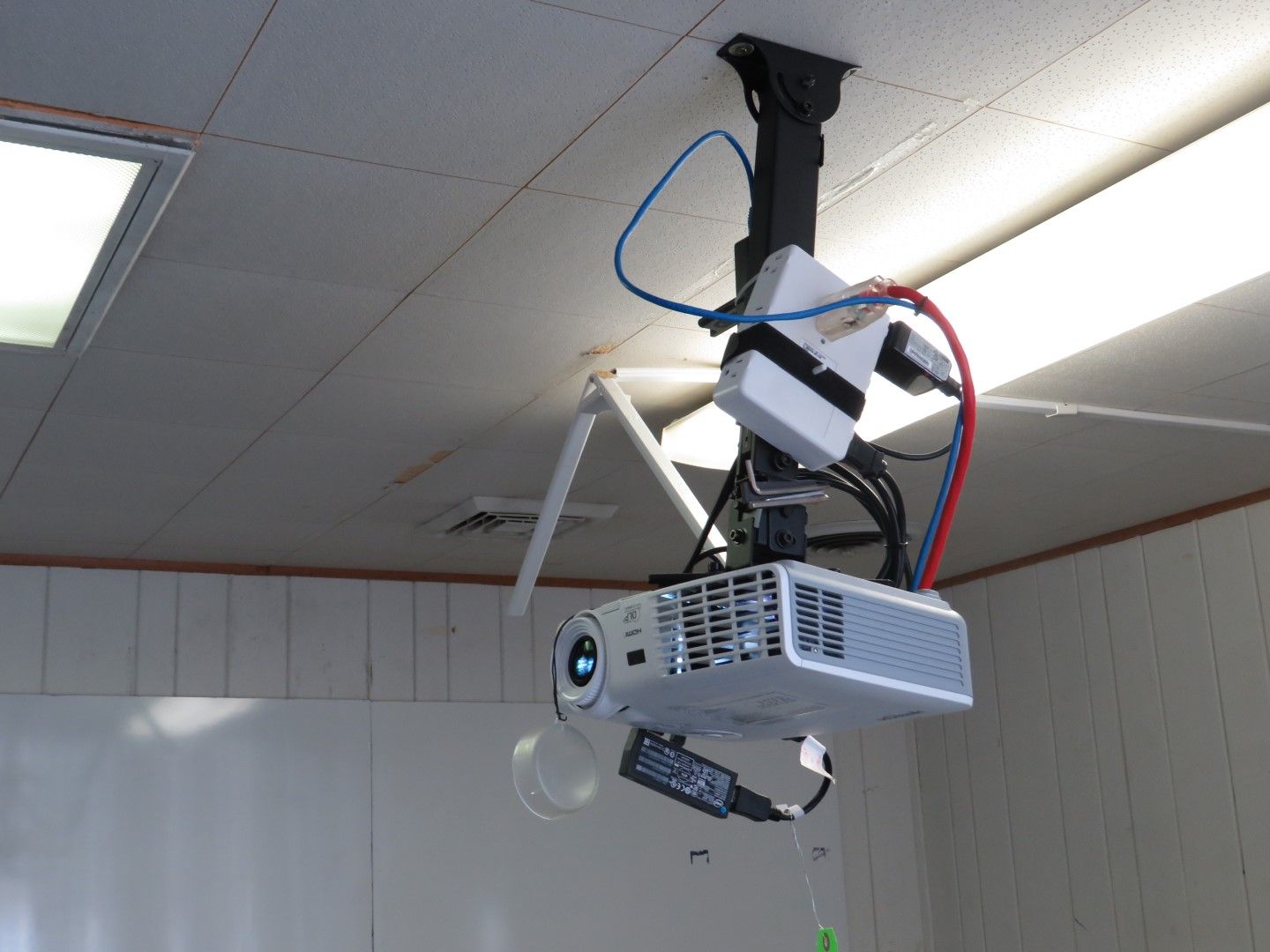 Ceiling-mounted projector with connected cables and device.  Projector is white and gray, mounted in a classroom setting.