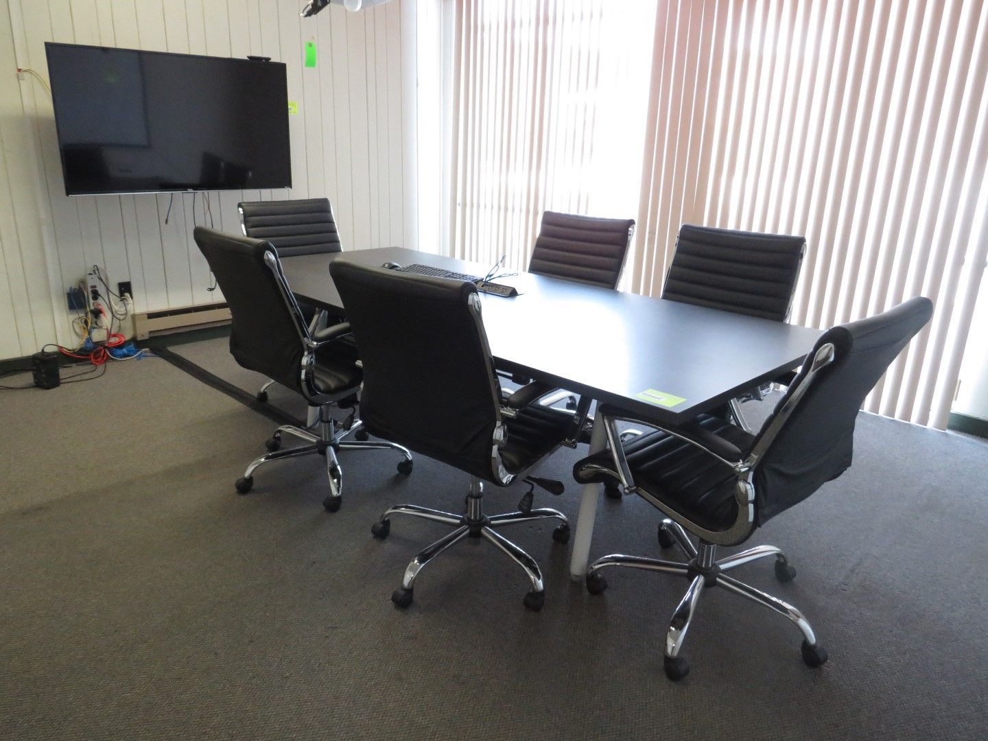 Conference room with large black table, six black chairs, TV on wall, and window with blinds.