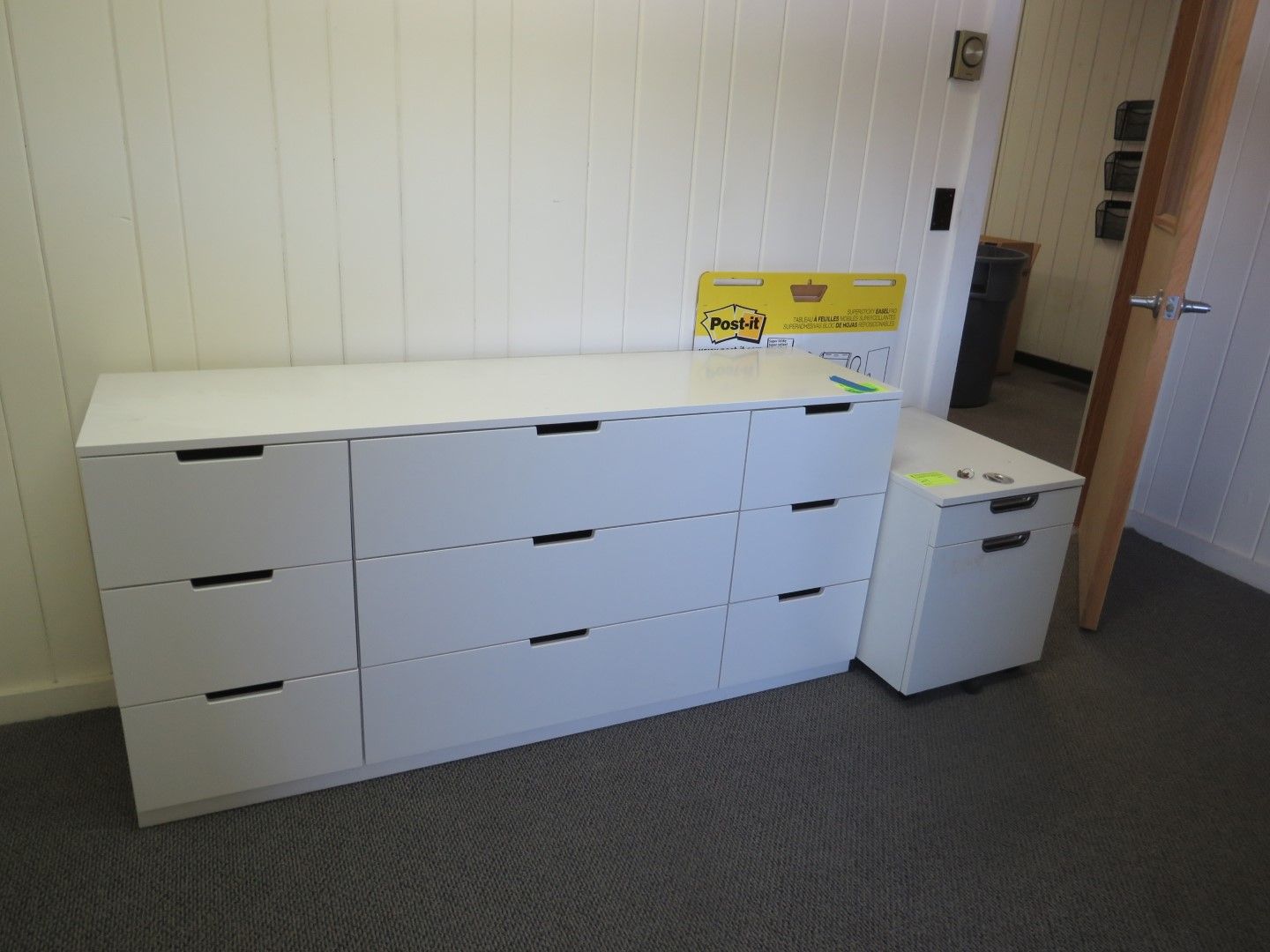 White dresser with black handles and matching rolling cabinet. Set against a white wall.