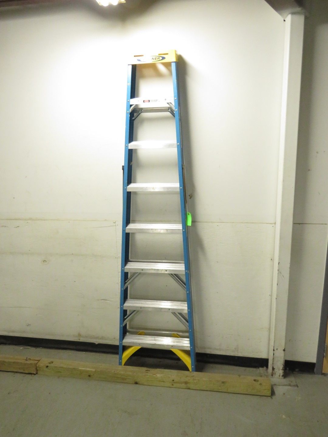Blue and silver ladder leaning against a white wall in a room.