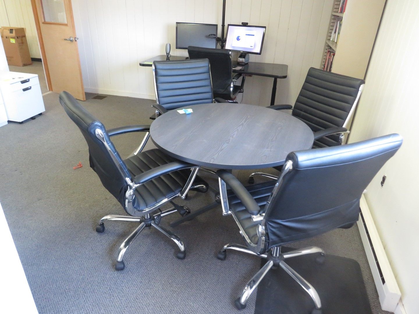 Round table with four black chairs in an office setting.