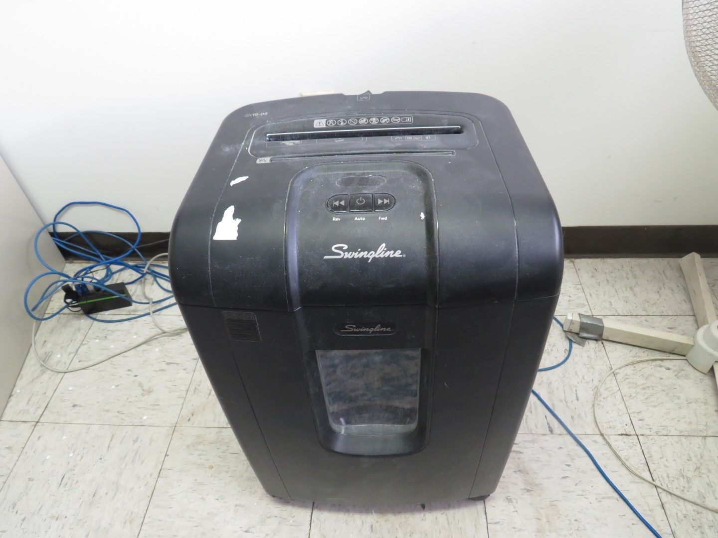 Black paper shredder in a room, with electrical cords visible.