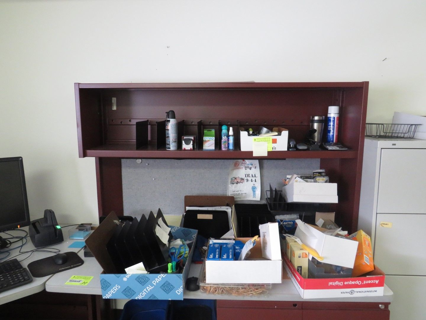 A desk with a shelf holding various items, with a file cabinet to the right.