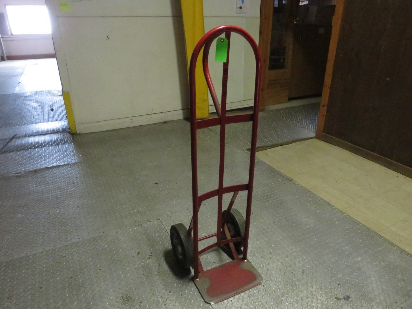 Red hand truck on a textured floor, in a room with light-colored walls and a doorway.