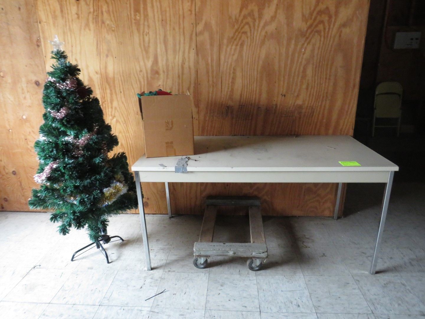 Christmas tree, table, box, and dolly against a wood wall.