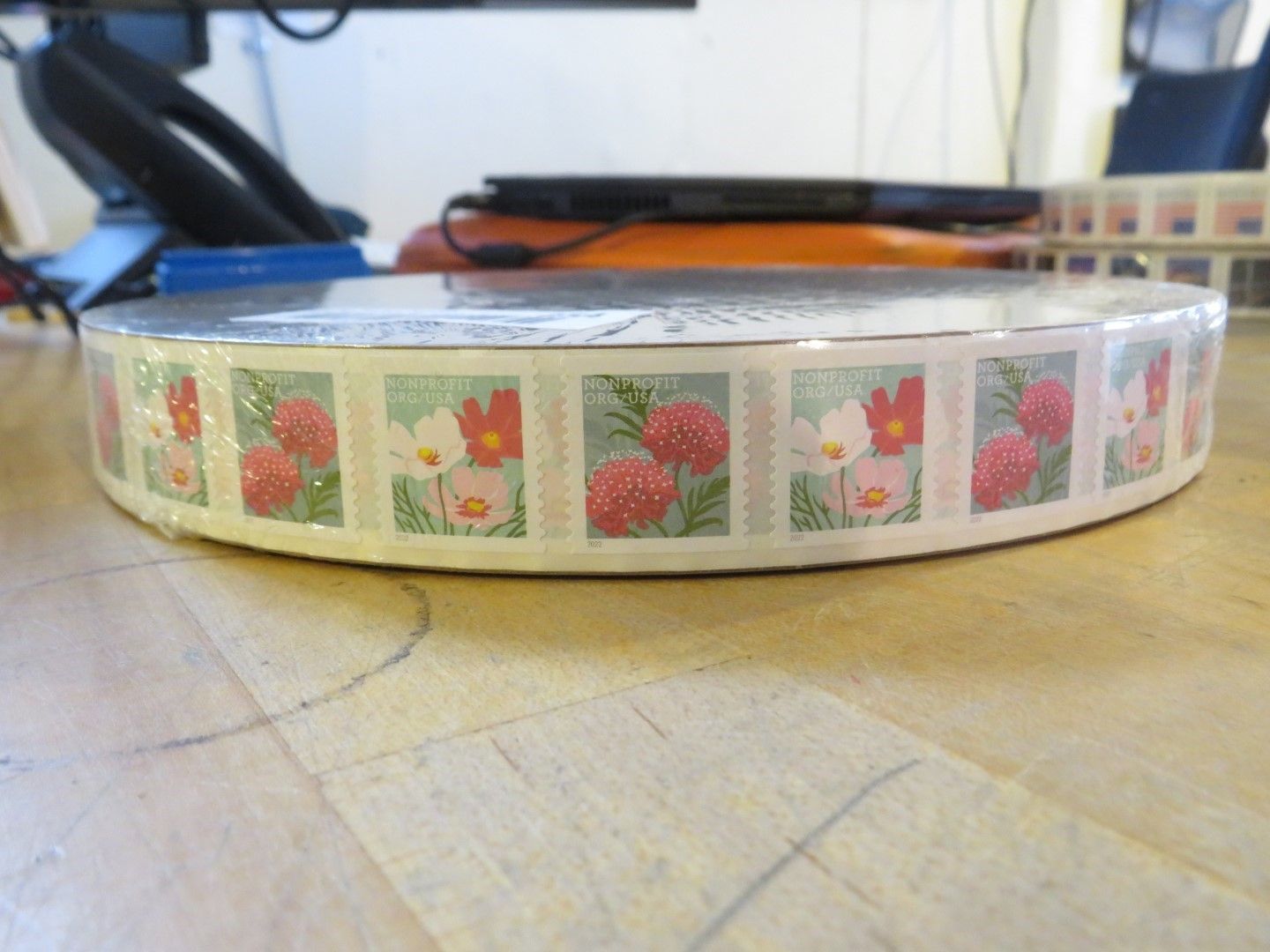 Roll of postage stamps featuring flowers, lying on a wooden surface.