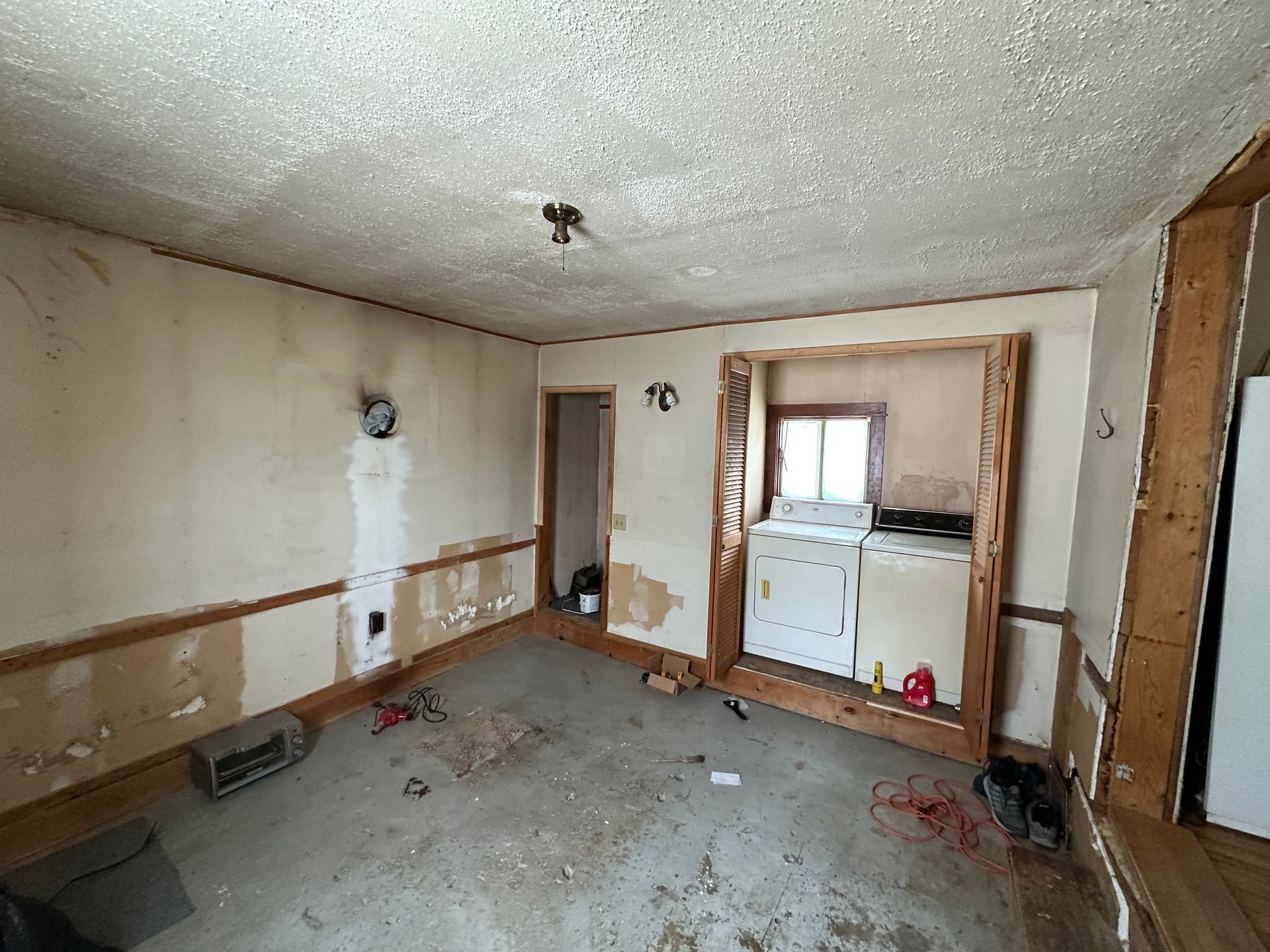 An interior room with bare walls, exposed wood trim, and a built-in laundry area with appliances.