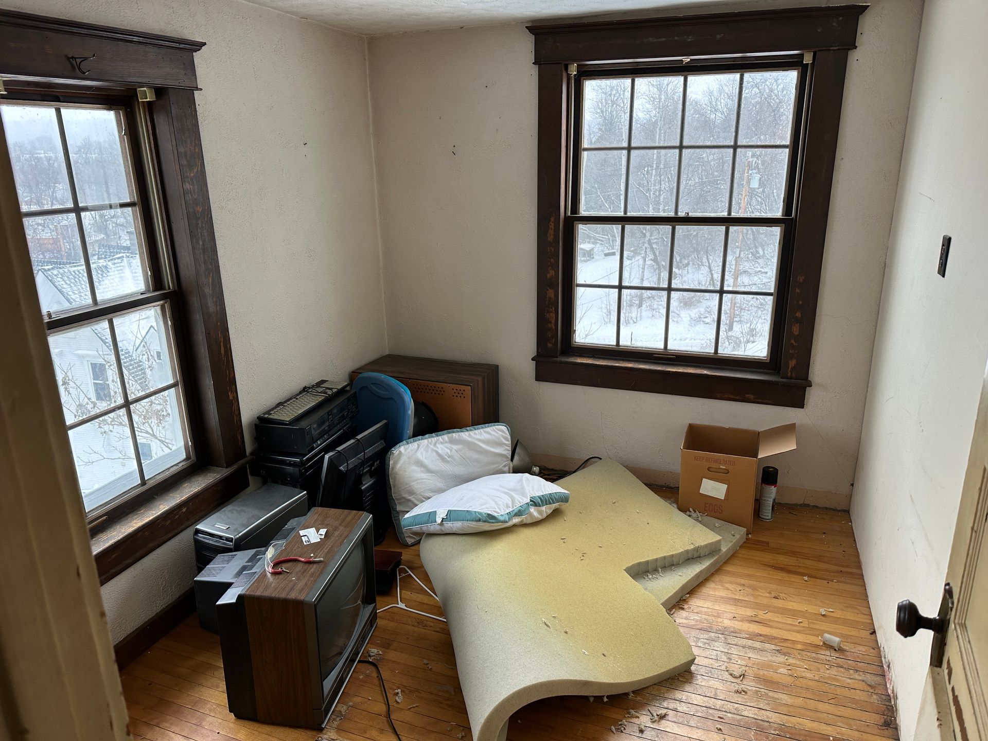 A small, empty room with hardwood floors, two windows.
