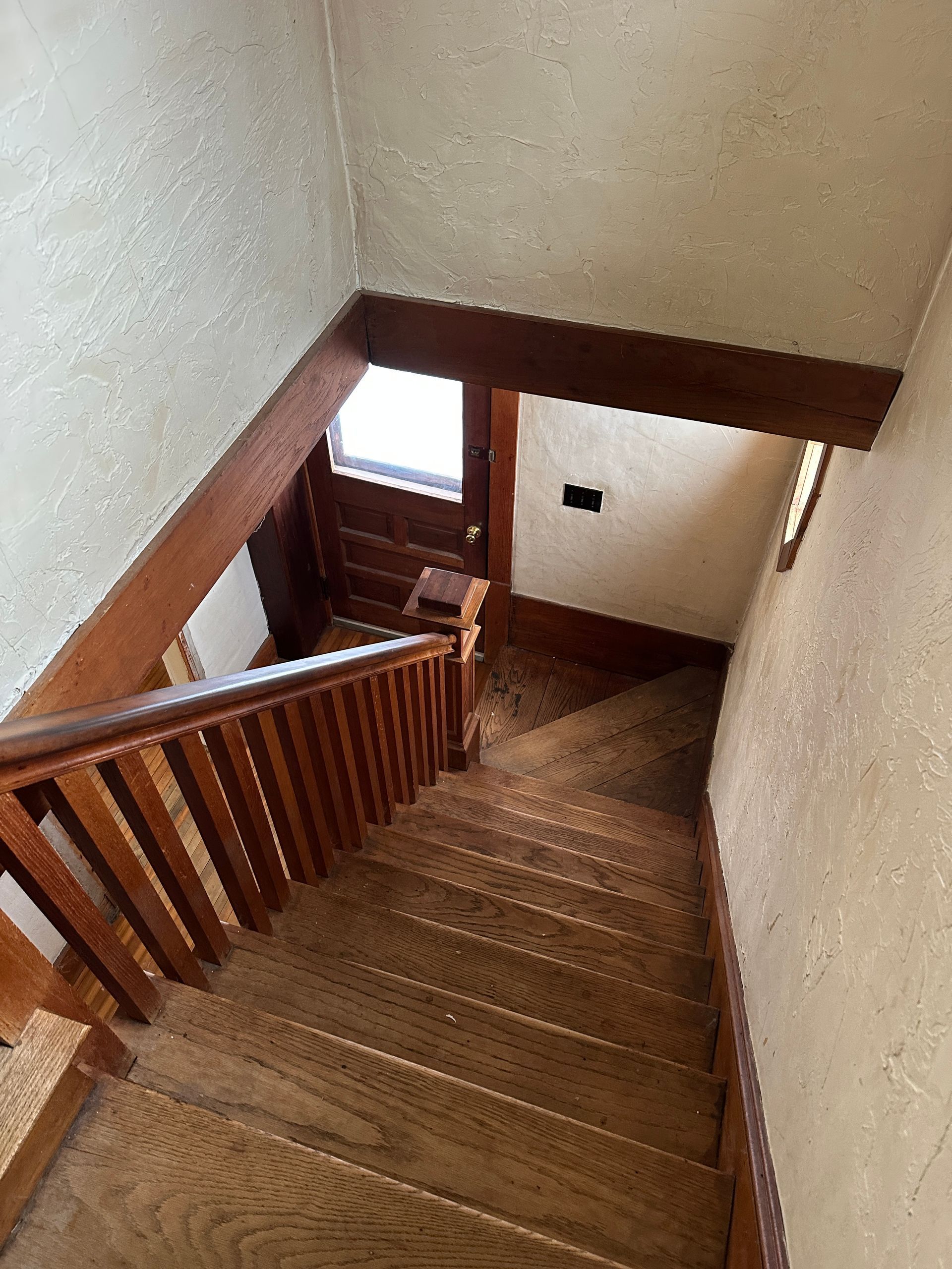 A view looking down a wooden staircase toward an entryway door with glass panes and dark wooden trim.