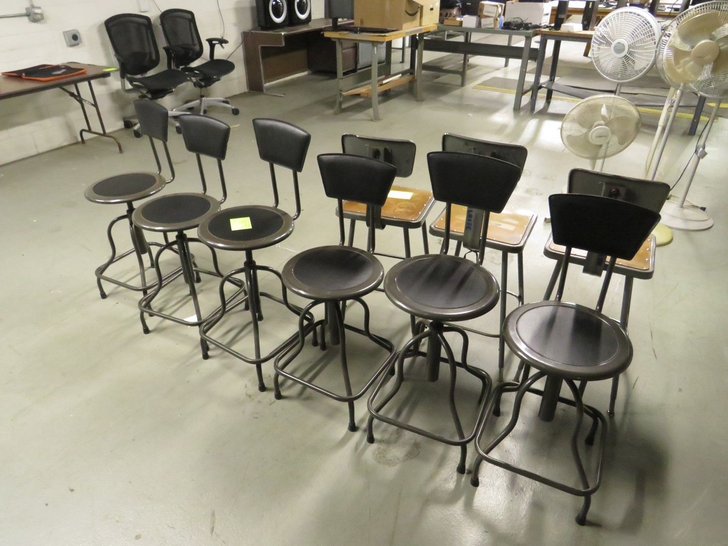 Row of industrial-style adjustable stools and chairs in a warehouse setting.