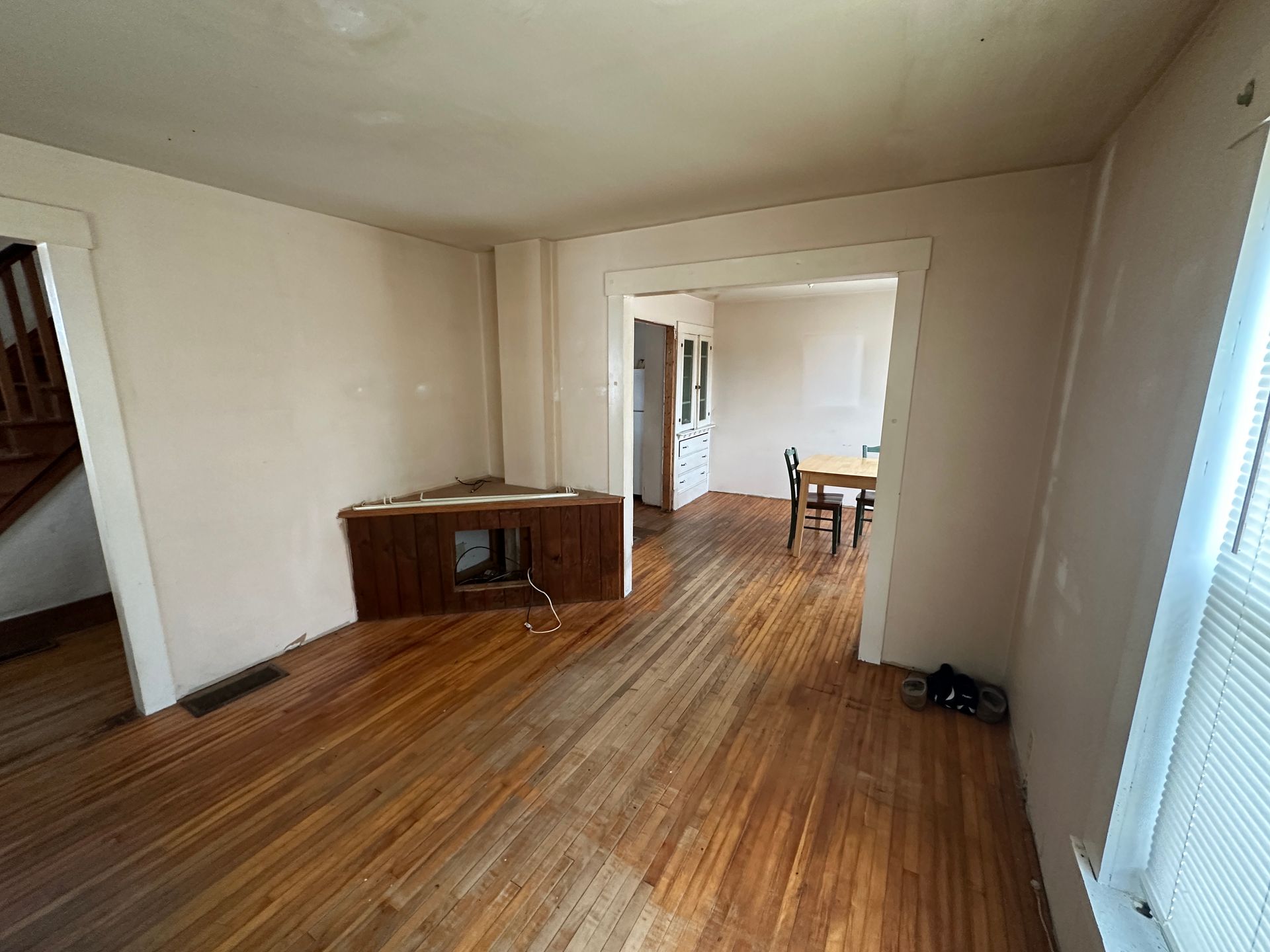 Empty living room with hardwood floors, a corner fireplace unit, and an open doorway leading to a dining area.