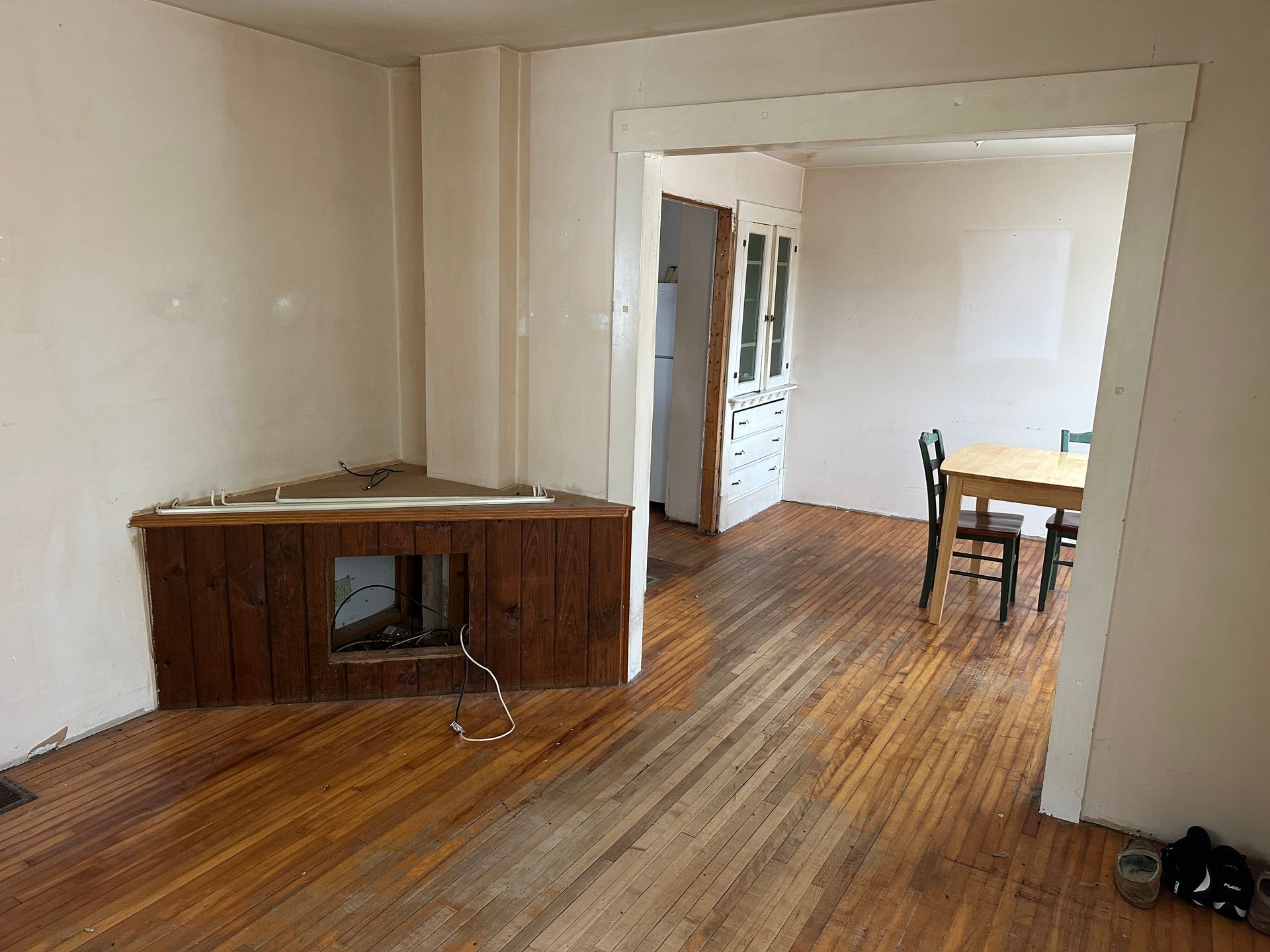 A room with hardwood floors, a corner fireplace with brown wood paneling, and a doorway leading to a dining area.