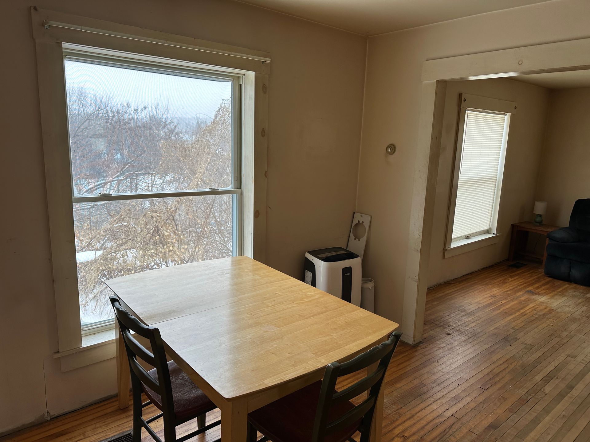 A light wood dining table with two chairs sits next to a large window in a room with hardwood floors.