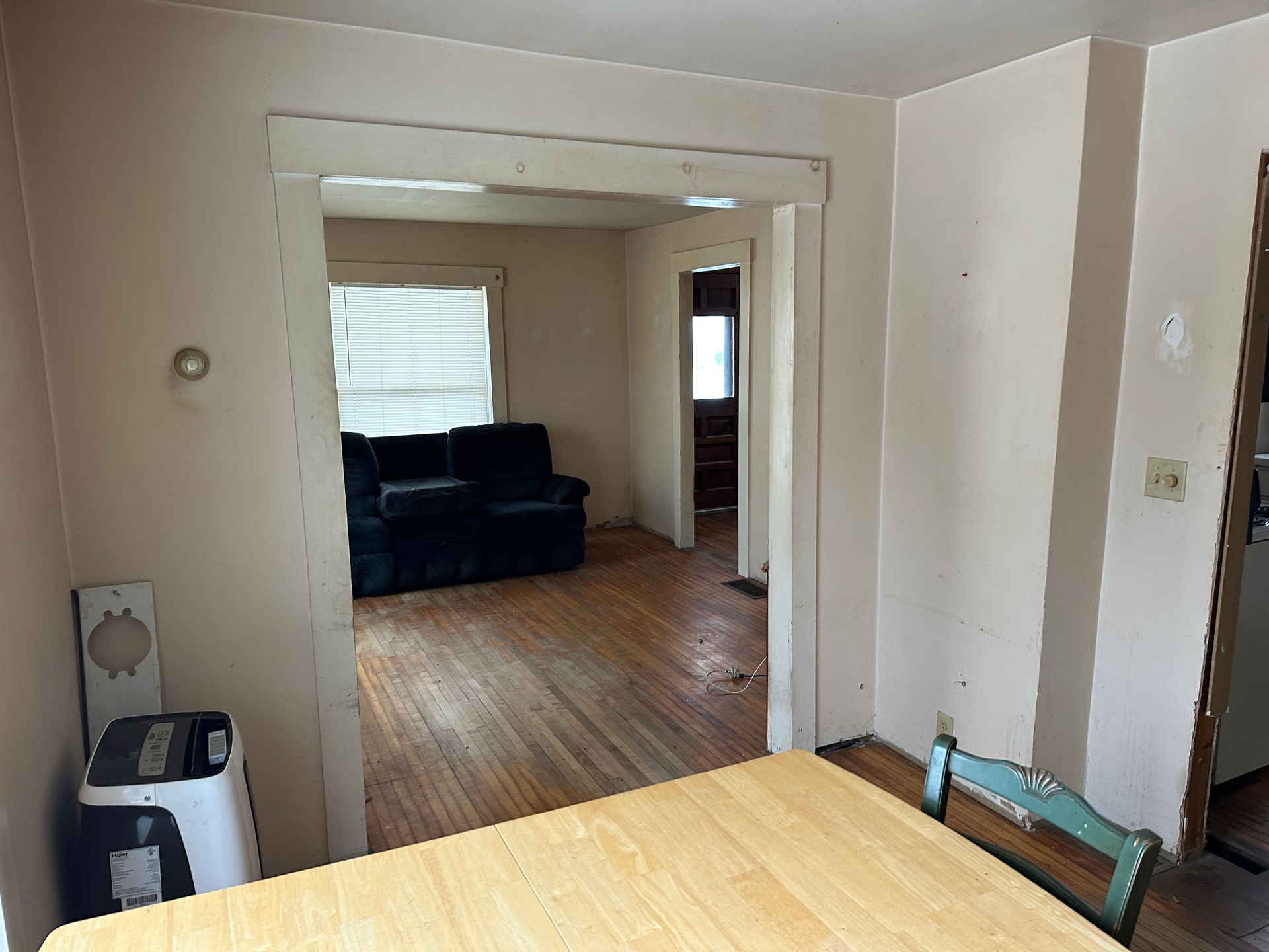 A dining room foreground looks through a wide doorway into a living room with hardwood floors and a dark blue sofa.