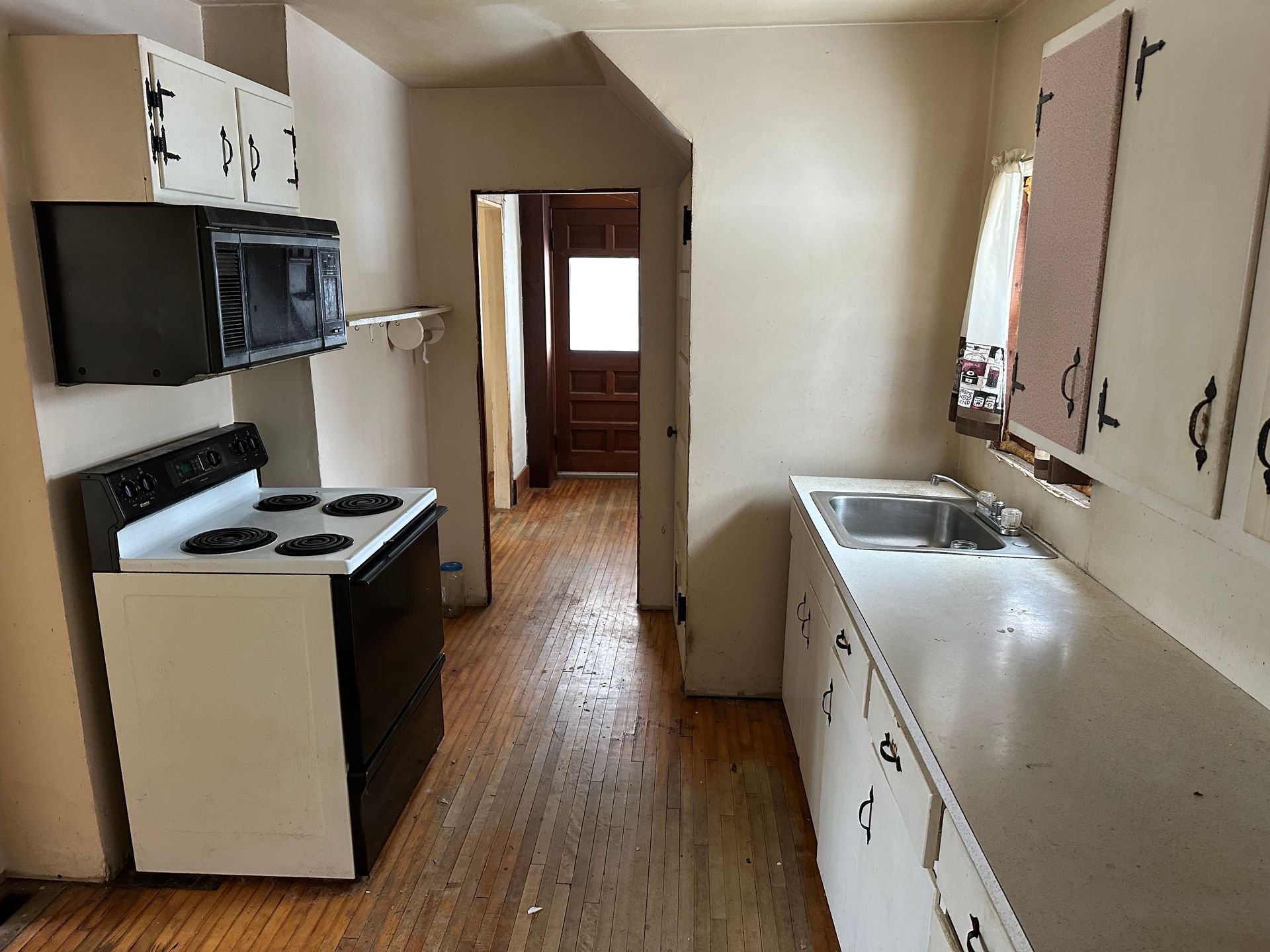 A kitchen featuring white cabinets, a black stove, a countertop with a sink, and a doorway leading to another room.