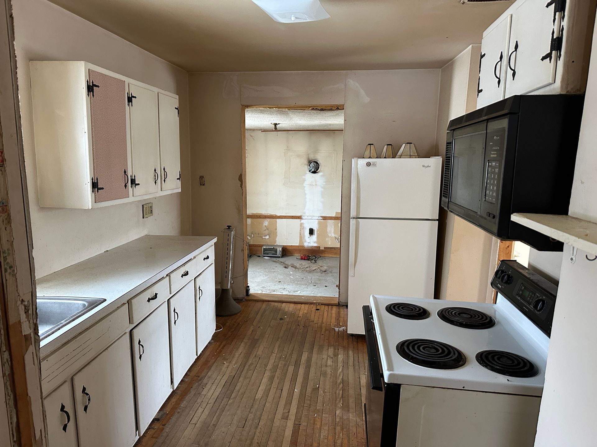 A kitchen features white cabinets, a stove, a microwave, and a white refrigerator, with an open doorway.